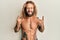 Handsome man with beard and long hair standing shirtless showing tattoos shouting with crazy expression doing rock symbol with