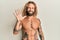 Handsome man with beard and long hair standing shirtless showing tattoos showing and pointing up with fingers number five while