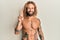 Handsome man with beard and long hair standing shirtless showing tattoos showing and pointing up with fingers number two while