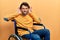 Handsome man with beard sitting on wheelchair trying to hear both hands on ear gesture, curious for gossip
