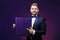 Handsome man with beard in tuxedo holds large box and smiling on