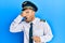 Handsome man with beard wearing airplane pilot uniform peeking in shock covering face and eyes with hand, looking through fingers