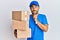 Handsome man with beard wearing courier uniform holding delivery packages with hand on chin thinking about question, pensive