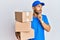 Handsome man with beard wearing courier uniform holding delivery packages with hand on chin thinking about question, pensive