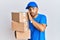 Handsome man with beard wearing courier uniform holding delivery packages hand on mouth telling secret rumor, whispering malicious