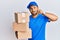 Handsome man with beard wearing courier uniform holding delivery packages mouth and lips shut as zip with fingers