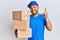 Handsome man with beard wearing courier uniform holding delivery packages pointing finger up with successful idea