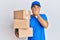 Handsome man with beard wearing courier uniform holding delivery packages shocked covering mouth with hands for mistake