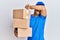 Handsome man with beard wearing courier uniform holding delivery packages smiling cheerful playing peek a boo with hands showing