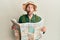 Handsome man with beard wearing explorer hat holding map making fish face with mouth and squinting eyes, crazy and comical