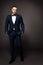 Handsome Man in Black Suit, Elegant Fashion Model Studio Portrait in Tuxedo, Hands in Pockets