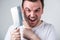 Handsome man grimaces and wants to shave stubble with a kitchen cleaver on a gray background