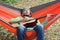 Handsome man hiker play on guitar while sitting in a hammock after trip in the autumn forest. Camping lifestyle concept