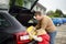 Handsome man and his little son going to vacations, loading their suitcase in car trunk. Automobile trip in the countryside.