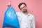 Handsome man holding blue garbage bag isolated on pink background