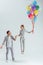 handsome man holding hand of woman jumping in air with bundle of colorful balloons