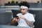 Handsome man holding modern smartphone dialing number, male with dreadlocks hair in white t-shirt using mobile phone for chatting