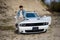 Handsome man in jeans jacket and cap sit on hood at his white muscle car in career