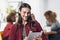 Handsome man with long hair smiling holding digital tablet with friends in background