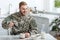 Handsome man in military uniform smiling and pouring coffee in cup from kettle