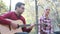 Handsome man playing guitar while beautiful woman sitting next to him in park