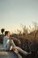 Handsome man posing in profile on bare feet sitting on wooden walkway on lake shore. Vertical portrait photography