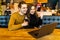 Handsome man and pretty woman making video call to their friend using free wi-fi on generic laptop pc, having meal, sitting at
