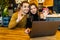 Handsome man and pretty woman making video call to their friend using free wi-fi on generic laptop pc, having meal, sitting at