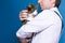 Handsome man in shirt and black suspenders holding and stroking cute grey cat in golden crown on blue background