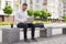 Handsome man sitting on bench, working on laptop outdoors.