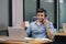 Handsome man speaking microphone with headset looking laptop holding coffee cup at table work in home office.