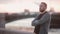 Handsome man standing on a quay, folding his arms on a chest. Man with a beard turns his head to camera and smiles