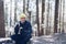 Handsome man tourist in yellow cap sitting on tree stump with metal cup of hot tea, hamburger resting on the trail