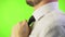 Handsome man in a white shirt straightens his tie on a green screen background. Close-up