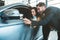 Handsome man and young beautiful woman looking happy checking new car interior while choosing new car in dealership