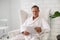 Handsome mature European man dressed in white bathrobe, with a blank paper sheet, sitting armchair in luxurious wellness spa