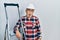 Handsome mature handyman close to construction stairs wearing hardhat in shock face, looking skeptical and sarcastic, surprised