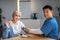 Handsome mature korean man doctor measures pressure with tonometer to senior female, patient waving hand