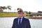 Handsome mature man, executive, grey hair, beard, sunglasses, jacket and tie, is in a park with an artificial lake posing for