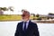 Handsome mature man, executive, grey hair, beard, sunglasses, jacket and tie, is in a park with an artificial lake posing for
