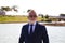 Handsome mature man, executive, grey hair, beard, sunglasses, jacket and tie, is in a park with an artificial lake posing for