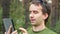 Handsome middle-age man in gren t-shirt sitting touch a tablet. He is smiling,summer forest on the background. Close-up