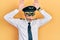 Handsome middle age man with grey hair wearing airplane pilot uniform doing bunny ears gesture with hands palms looking cynical