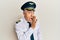 Handsome middle age mature man wearing airplane pilot uniform hand on mouth telling secret rumor, whispering malicious talk