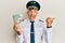 Handsome middle age mature man wearing airplane pilot uniform holding dollars pointing thumb up to the side smiling happy with