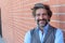 Handsome middle age Mediterranean man in a studio portrait on a red brick wall background smiling with copy space