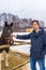 Handsome middle-aged man patting horse at ranch in snowy day. Winter weekend at farm, trip to countryside. Healthy lifestyle,