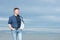 Handsome middle-aged man walking at the beach. Attractive mid adult male model posing at seaside in blue jeans, t-shirt shirt.