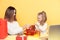 Handsome mother with little daughter unpaking gifts sitting isolated over the yellow background.