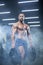 Handsome muscular athlete man is standing in a gym against the background of smoke holding barbell discs in both hands